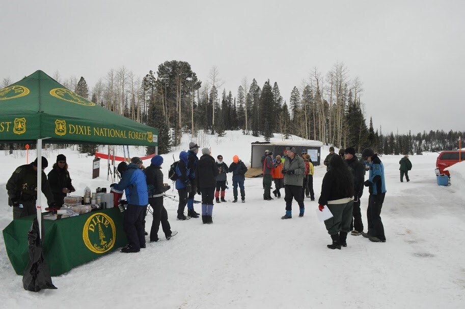 Skiers and Forest Service staff gathered in the snowy Deer Hollow parking area beside a Dixie National Forest tent