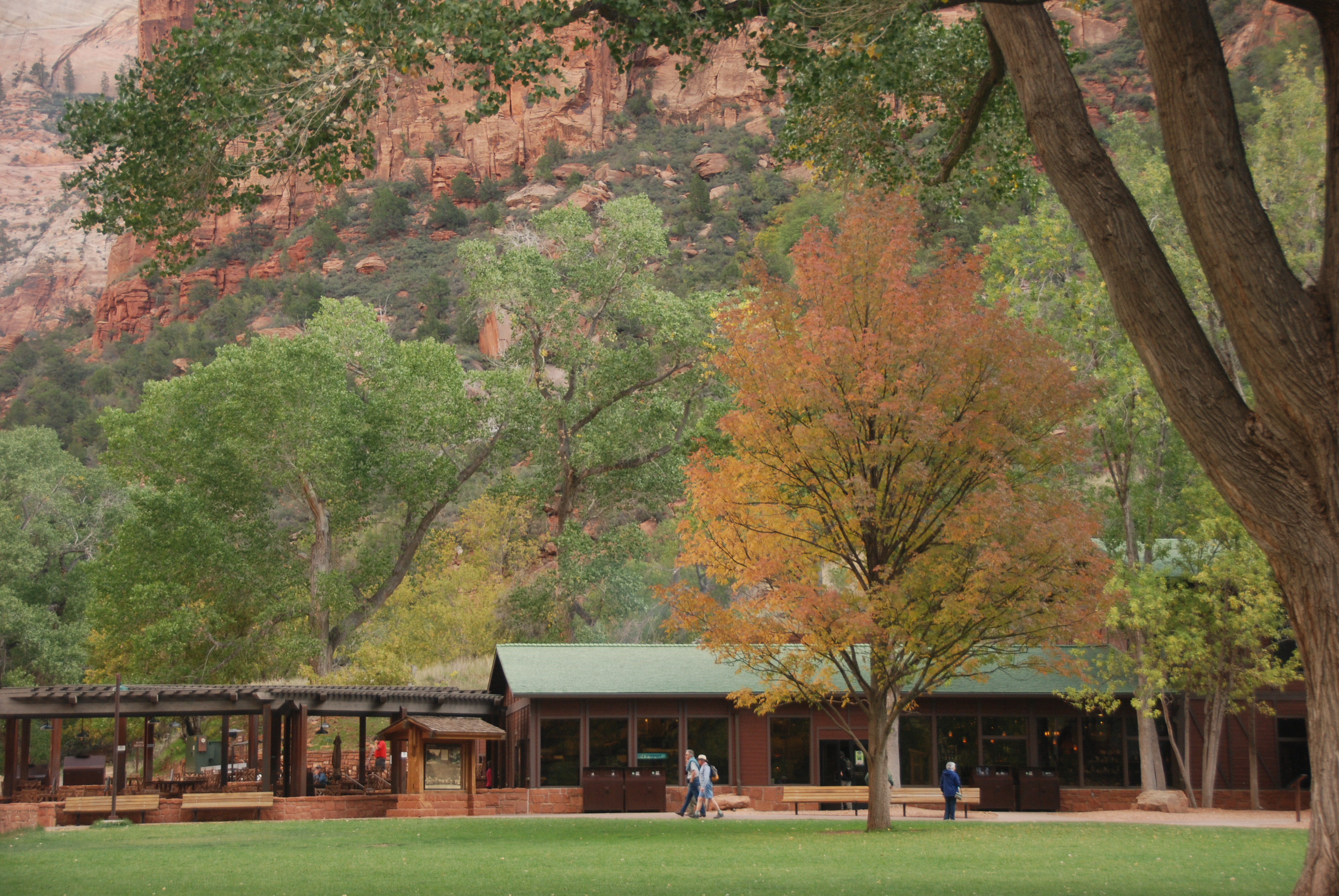Zion Lodge and its lawn framed by early fall color beneath the red canyon wall