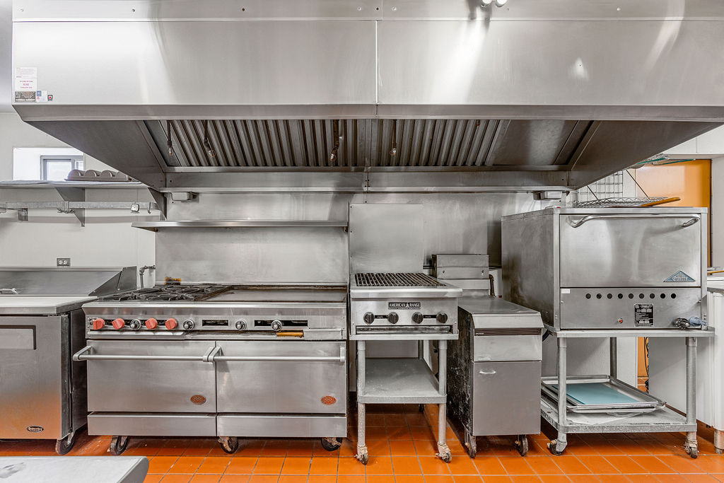 Commercial kitchen with stainless steel range, grill, and convection oven for group meals during a hotel buyout.