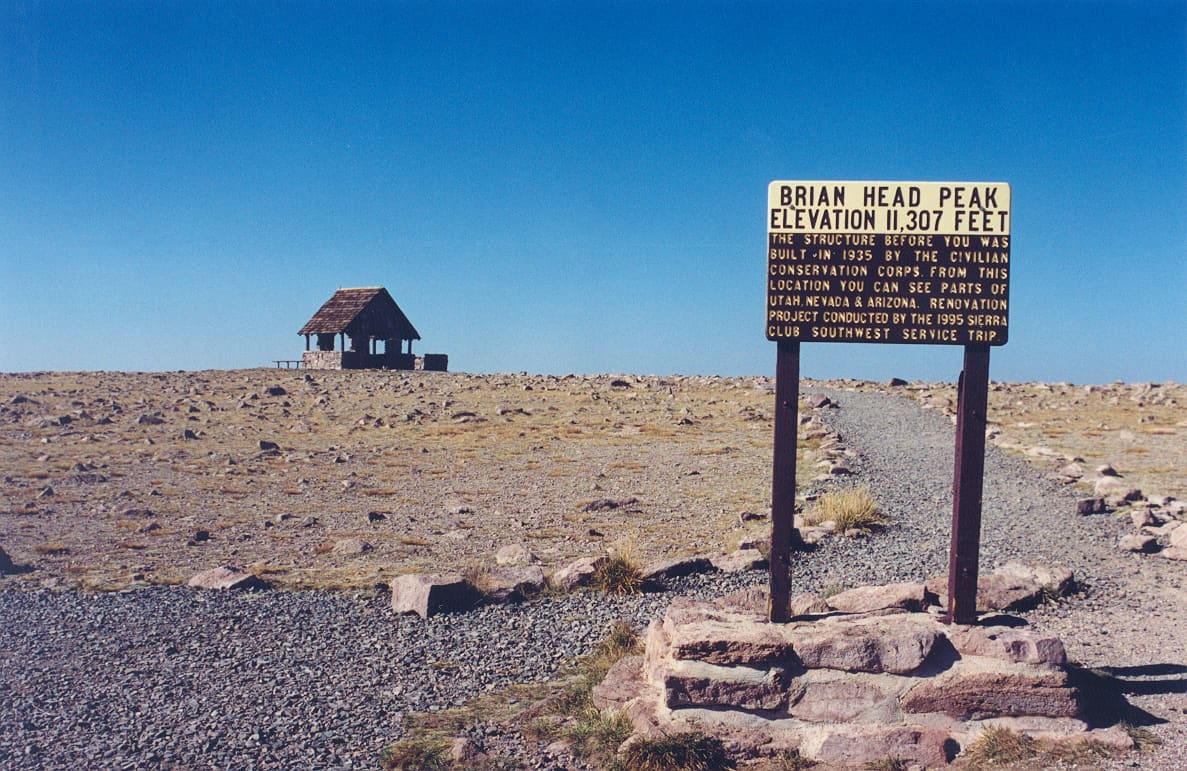 The stone and timber observation shelter on the summit of Brian Head Peak beside an interpretive sign reading Brian Head Peak, elevation 11,307 feet