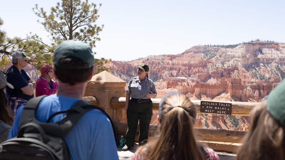 A ranger in uniform talks to visitors on the rim at Sunset Point (NPS photo)
