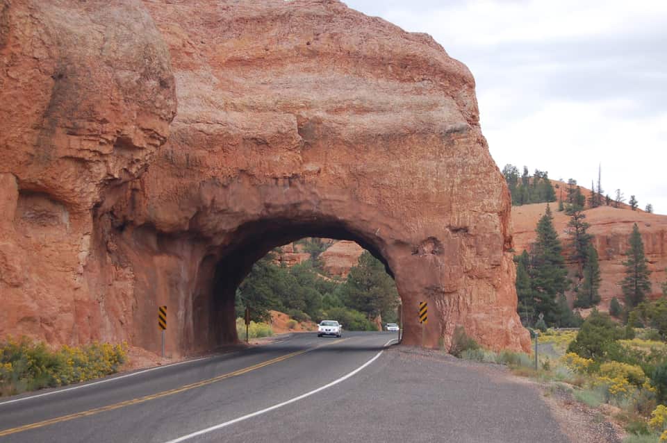 A car passing through a rock arch tunnel on Scenic Byway 12 in Red Canyon