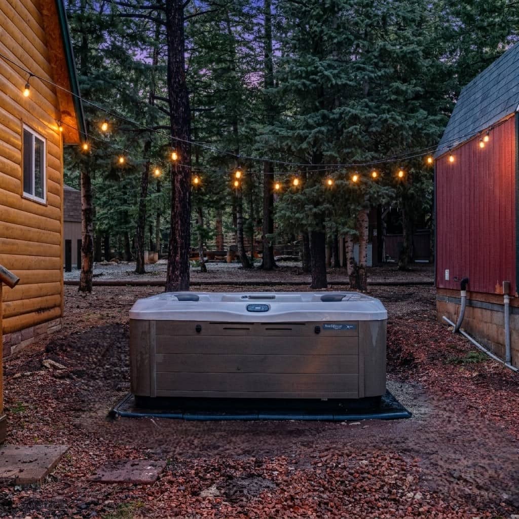 Private hot tub under string lights at dusk at Forest Haven Cabin