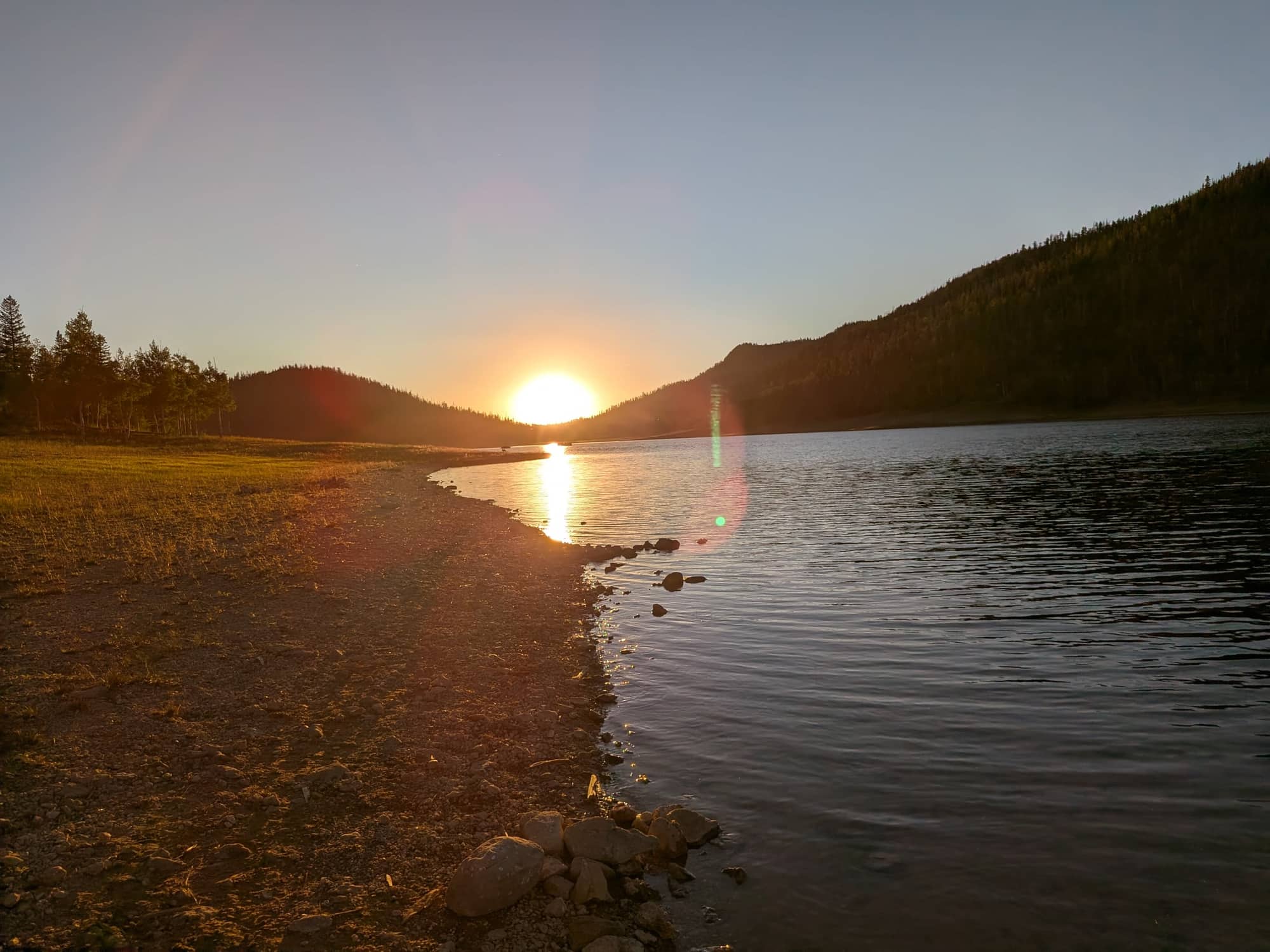 Sunset over Navajo Lake from the south shore, with the far ridge dark against an orange sky