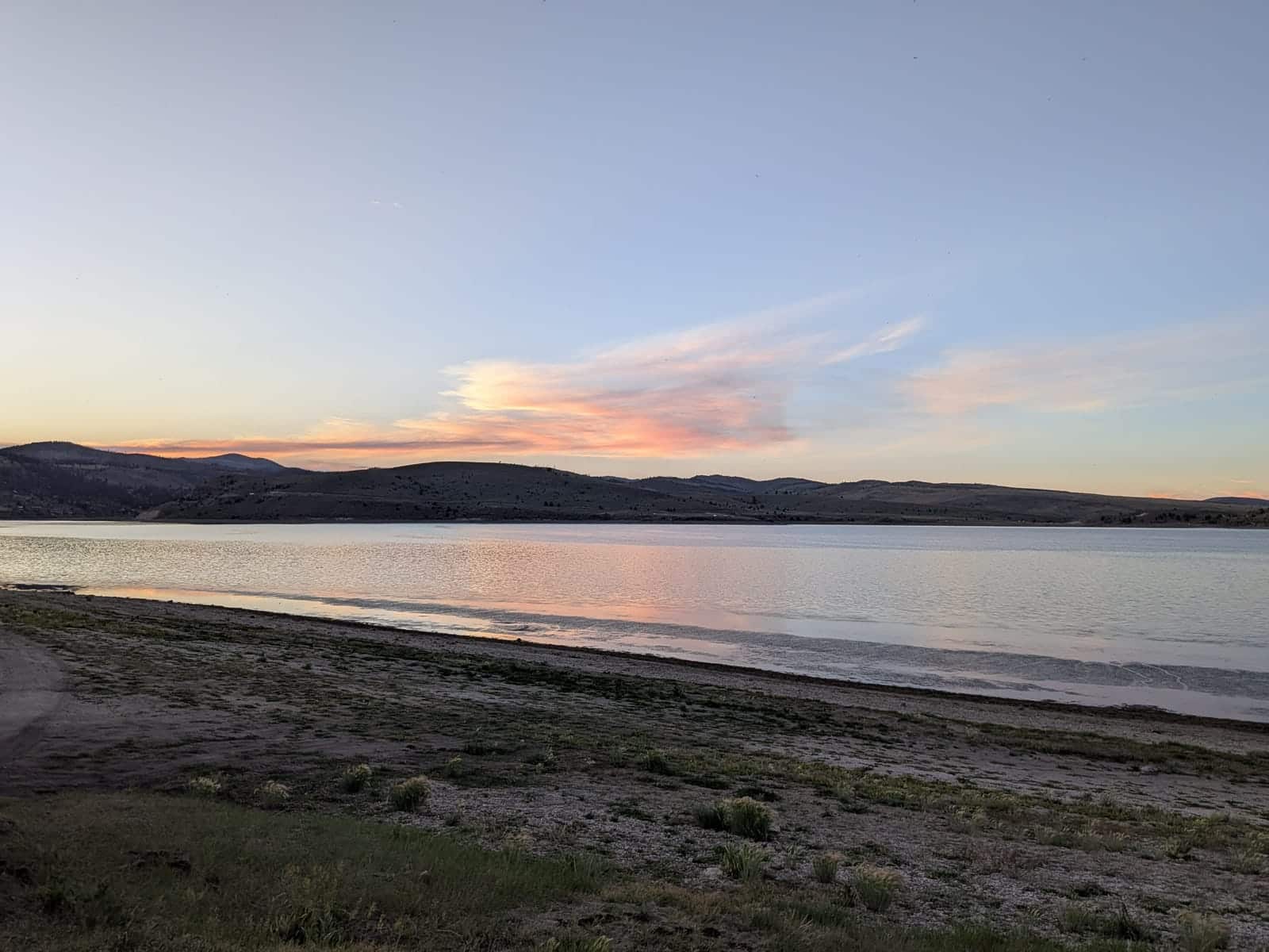 Panguitch Lake at sunset with a wide shoreline in the foreground and low hills reflected in calm water