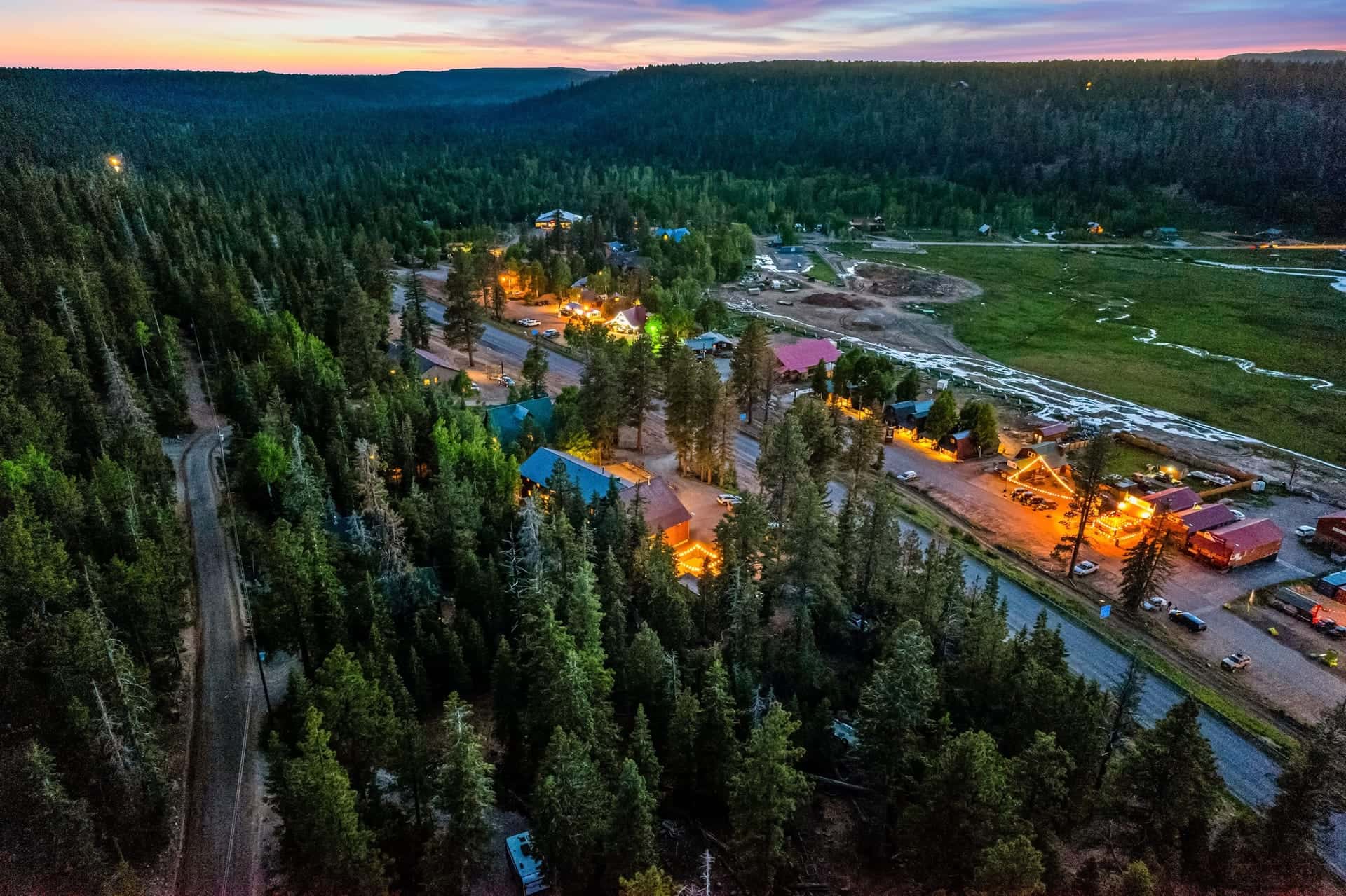 Aerial view of Duck Creek Village at dusk, lit cabins among the pines below the plateau