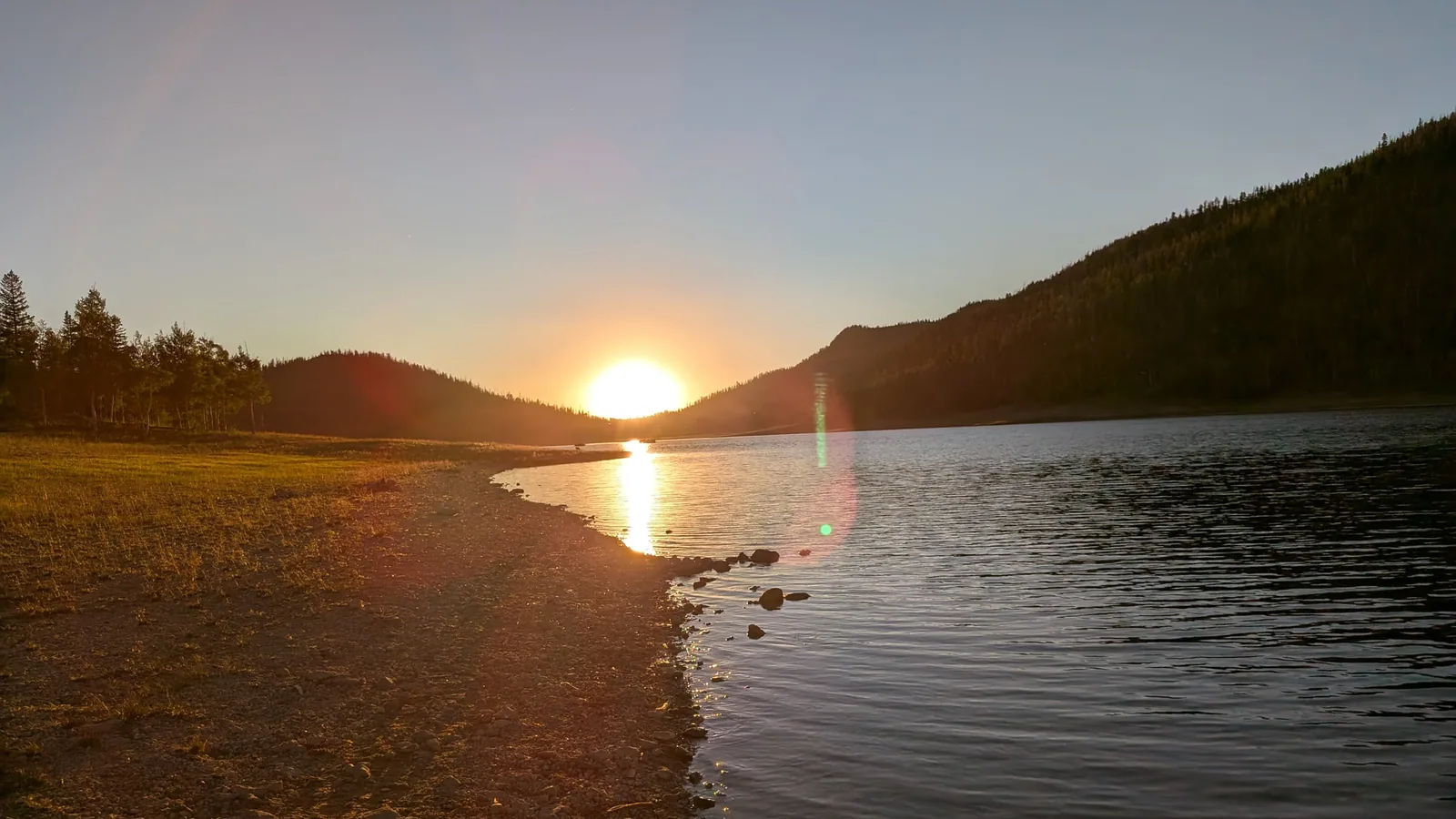 Le soleil se couchant sur l'eau calme et la rive rocheuse du lac Navajo par un soir d'été, avec des collines boisées de chaque côté