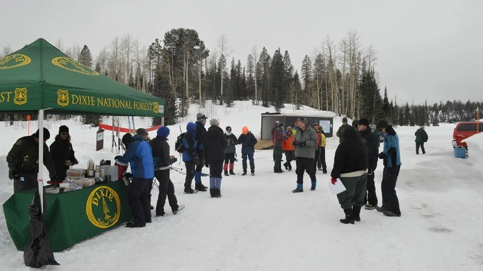 Snowshoers and skiers gather at the snowy Deer Hollow trailhead on the Dixie National Forest under a gray February sky, aspens and spruce behind them