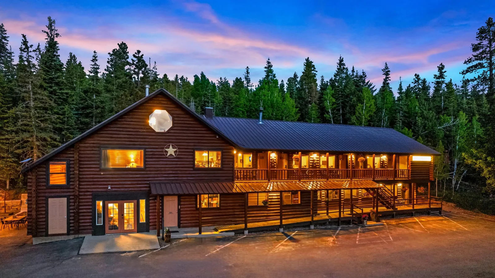 Duck Creek Village Inn, un lodge de troncos de dos plantas, iluminado al anochecer bajo un cielo rosado con altos pinos detrás