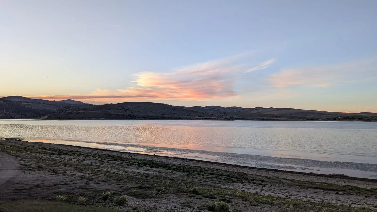 日落时分的潘吉奇湖，前景是开阔的砾石湖岸，对岸是低矮的山丘