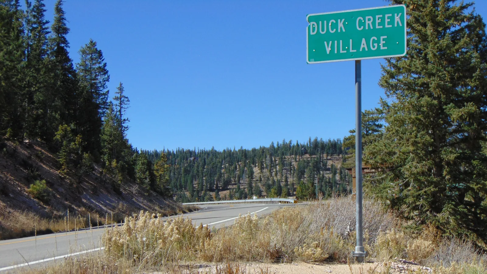 State Route 14 curving past the Duck Creek Village highway sign through the pines of the Markagunt Plateau