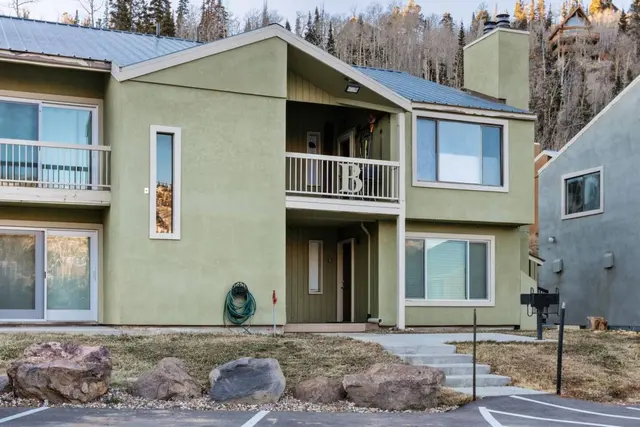 Two-story sage-green condo building with balconies and parking in front