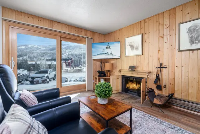 Knotty pine living room with a leather sofa, a fireplace and a big window looking out at snowy slopes
