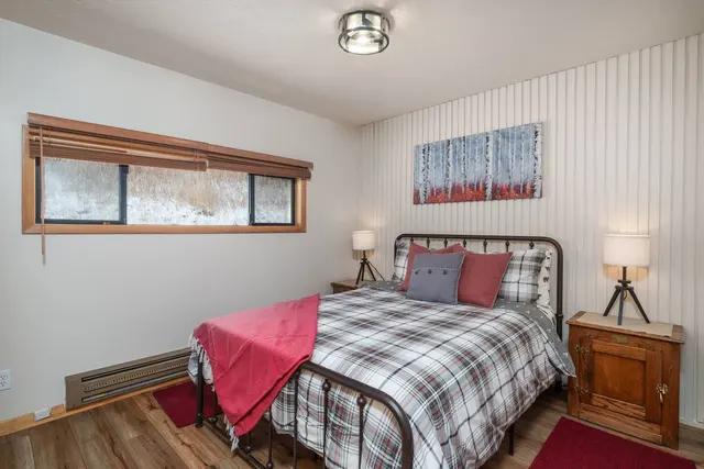 Second bedroom with a queen bed, a red throw and birch-tree art